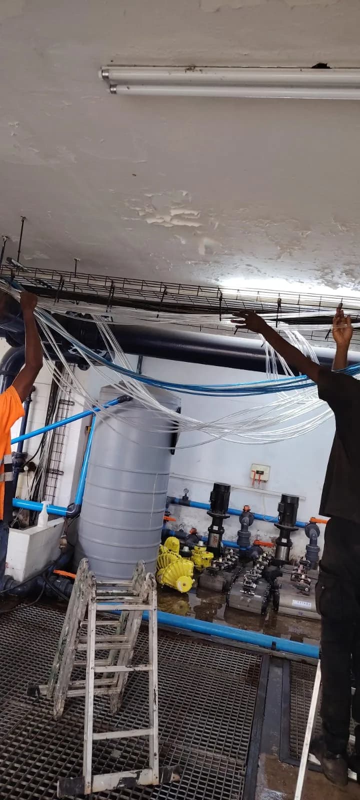 Two technicians raising airline runs above staged actuated valves and dosing pumps