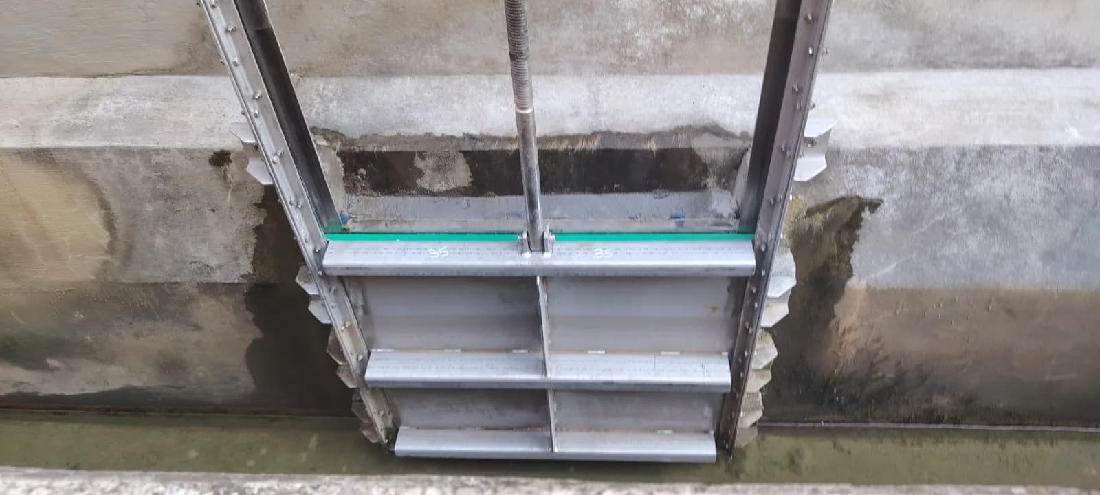 The re-engineered stainless steel sluice gate — twin spindles and toothed guides — installed in the concrete channel
